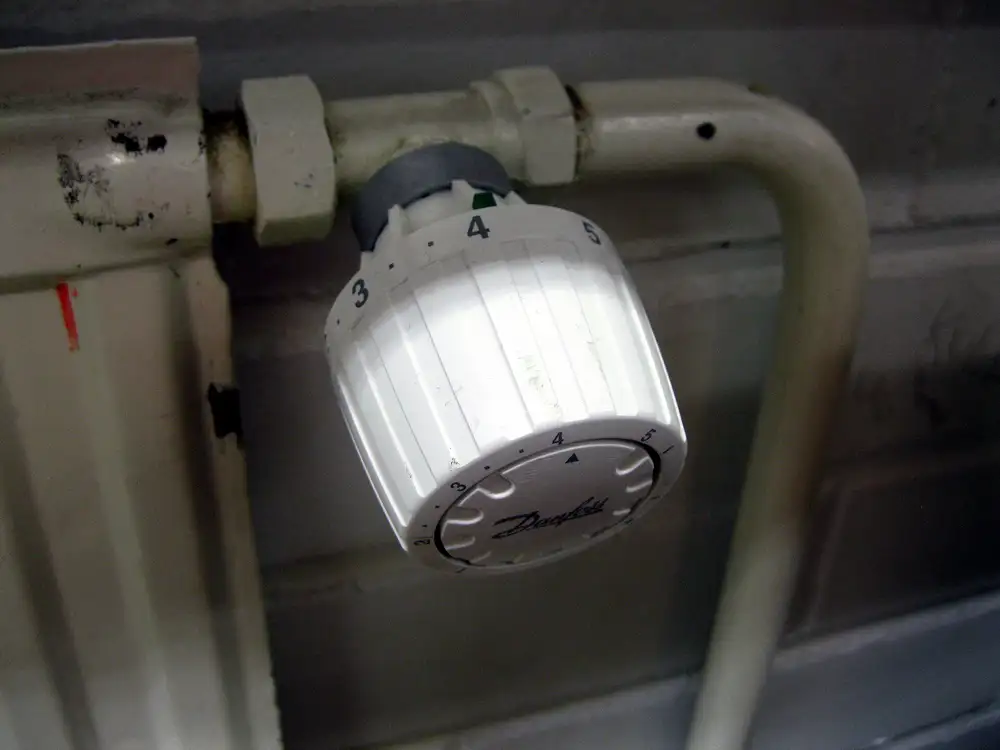 Cabezal blanco de una válvula termostática con su escala numerada, montado en la tubería de un radiador